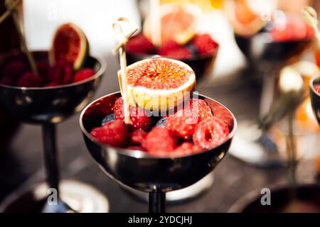 Eine polierte silberne Schüssel ist mit einer Vielzahl frischer Beeren und Feigen gefüllt. Leckerer Obstsnack am Buffet. Ein stilvolles Dessertangebot für eine Spezialität Stockfoto
