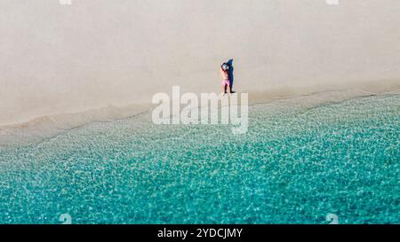 Ein Blick aus der Luft auf einen jungen Mann mit weißem Hut am Meer. Ein Mann genießt die Meereslandschaft. Ein Mann entspannt sich an einem sauberen Sandstrand. Urlaub und Reise Stockfoto