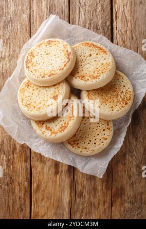 Frisch zubereitete englische Crumpets aus Nahaufnahme auf Pergamentpapier auf dem Tisch. Vertikale Draufsicht von oben Stockfoto