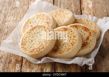 Poröse hausgemachte englische Crumpets aus Nahaufnahme auf Pergamentpapier auf einem alten Tisch. Horizontal Stockfoto