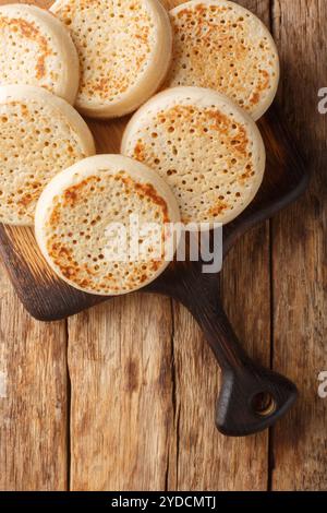 Crumpets frisch aus einer Bäckerei auf dem Holzbrett auf dem Tisch. Vertikale Draufsicht von oben Stockfoto