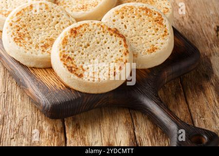 Köstliche heiße englische Crumpets oder poröses Brot in Nahaufnahme auf Holzbrett auf dem Tisch. Horizontal Stockfoto