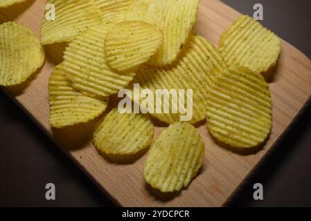 Fastfood, nicht gesundes Essen für die menschliche Gesundheit. Dünne Kartoffelscheiben und Wellpappe befinden sich auf einem hellen Holzhintergrund. Stockfoto