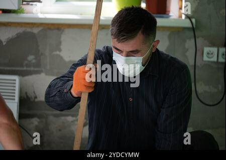 Ein Mann in einer Maske auf dem Hintergrund einer Wand aus Blöcken führt Reparaturarbeiten durch, eine minimale Schutzmaske gegen Schießpulver. Stockfoto