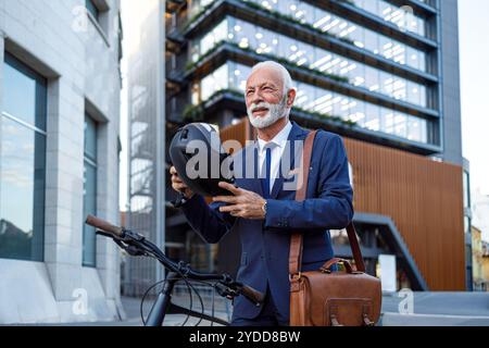Senior männlicher Pendler, der Helm aufsetzt, während er auf der Straße vor dem modernen Gebäude steht Stockfoto