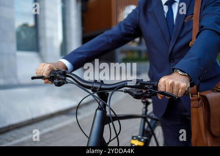 Mittelteil eines älteren männlichen Pendlers, der den Lenker hält und sein Fahrrad auf der Straße nach dem Büro schiebt Stockfoto