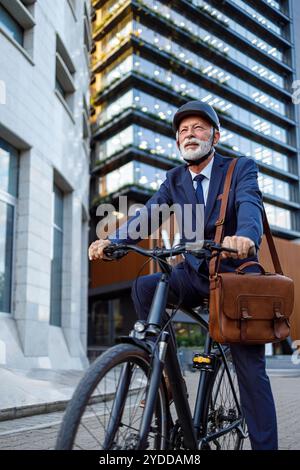 Niedriger Blickwinkel auf einen bärtigen alten Geschäftsmann mit Helm, der Fahrrad fährt und zum Büro in der Stadt reist Stockfoto