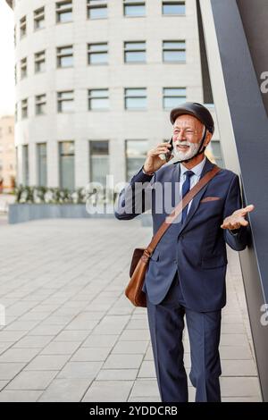 Leitender Helm, der über das Smartphone diskutiert, während er auf dem Fußweg in der modernen Stadt steht Stockfoto