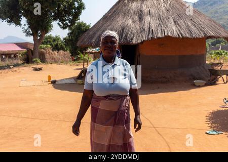 Frau, die vor einer traditionellen afrikanischen Lehmhütte steht, gebaut aus Lehm und Heu Stockfoto