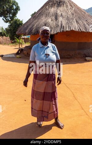 Frau, die vor einer traditionellen afrikanischen Lehmhütte steht, gebaut aus Lehm und Heu Stockfoto