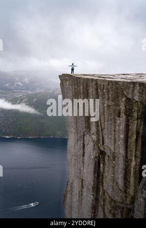 Eine Frau mit ausgestreckten Armen am Rande der Preikestolen Klippe, auch bekannt als Kanzel Rock, im Lysefjord in Norwegen an einem regnerischen Tag. Nein Stockfoto