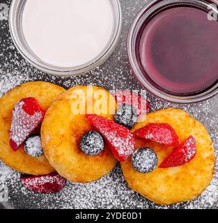 Hüttenkäsepfannkuchen mit Beeren, Puderzucker, Marmelade und Sauerrahm auf schwarzer Platte Stockfoto