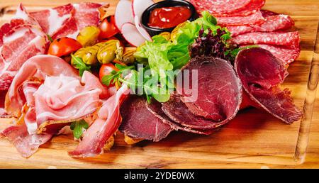 Verschiedene Fleischsorten, Würstchen, Salami, Schinken, Oliven, auf einem Holzbrett Stockfoto