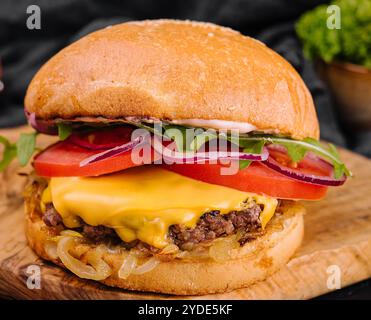 Leckerer gegrillter, hausgemachter Burger mit Rindfleisch, Tomaten, Käse, Zwiebeln und Salat. Stockfoto