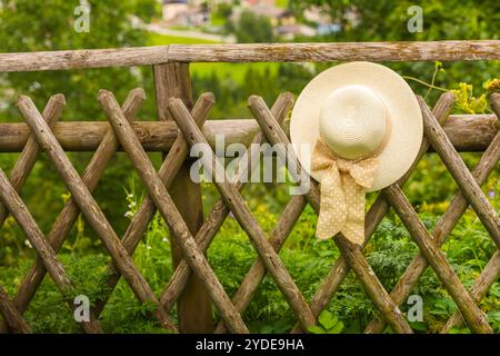 Weibliche Sommerhut hängt am hölzernen rustikalen Zaun Stockfoto