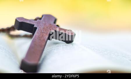 Dunkelrotes Holzkreuz, das sich an ein altes offenes Buch lehnt, das die Verbreitung der Liebe Jesu Christi unter Christen symbolisiert, die den Glauben und die Hingabe widerspiegelt Stockfoto