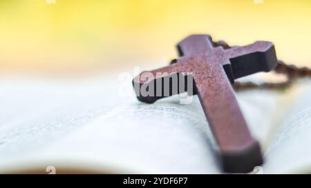 Dunkelrotes Holzkreuz, das sich an ein altes offenes Buch lehnt, das die Verbreitung der Liebe Jesu Christi unter Christen symbolisiert, die den Glauben und die Hingabe widerspiegelt Stockfoto