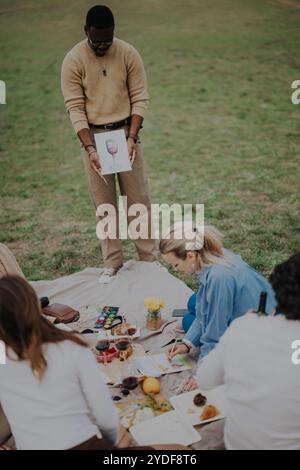 Eine Gruppe von Leuten, die einen Kunstkurs im Freien bei einem Picknick während des Malens genießen. Stockfoto