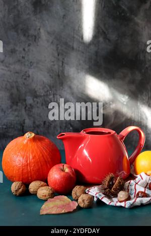 Rote dampfende Teekanne aus der Nähe. Heißer Tee in einem Topf und hausgemachte Kekse auf einem Tisch. Dunkler Hintergrund mit Kopierraum. Warmer Winterabend Stockfoto