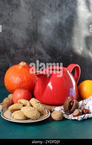 Rote dampfende Teekanne aus der Nähe. Heißer Tee in einem Topf und hausgemachte Kekse auf einem Tisch. Dunkler Hintergrund mit Kopierraum. Warmer Winterabend Stockfoto