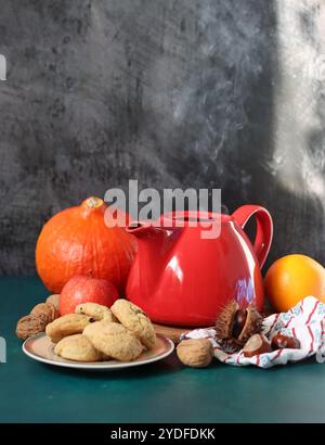 Rote dampfende Teekanne aus der Nähe. Heißer Tee in einem Topf und hausgemachte Kekse auf einem Tisch. Dunkler Hintergrund mit Kopierraum. Warmer Winterabend Stockfoto