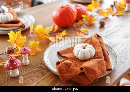 Wunderschön gestalteter Esstisch mit weißen und orangen Kürbissen, herbstgelben Blättern, Einrichtung mit eleganten Servietten, die auf Tellern auf braunem Holz gefaltet sind Stockfoto