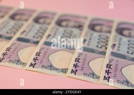 Japanische 5000-Yen-Scheine diagonal mit selektivem Fokus auf einer pastellrosa Oberfläche, die eine lebendige Komposition von Währungen schafft Stockfoto