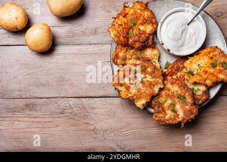 Kartoffellatkes mit Sauerrahm auf hölzernem Hintergrund, Draufsicht, Kopierraum. Traditionelle jüdische Latkes oder Levivot. Kartoffelrösti. Stockfoto
