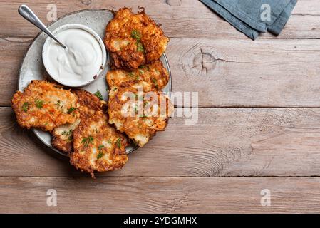 Kartoffellatkes mit Sauerrahm auf hölzernem Hintergrund, Draufsicht, Kopierraum. Traditionelle jüdische Latkes oder Levivot. Kartoffelrösti. Stockfoto