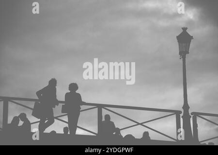 Silhouetten von Menschen im Nebel auf der Brücke bei Sonnenuntergang in Paris (Frankreich). Schwarzweißfoto. Stockfoto
