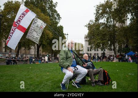 London, Großbritannien. Oktober 2024. Zwei Demonstranten sitzen während des Protestes auf dem Parlamentsplatz. Anhänger des ehemaligen Anführers der English Defence League (EDL) Tommy Robinson, dessen richtiger Name Stephen Yaxley-Lennon ist, schlossen sich dem Protest der Vereinigung des Königreichs in London an, während sich am North End von Whitehall in London ein Gegenprotest von Stand Up to Racism sammelt. Quelle: SOPA Images Limited/Alamy Live News Stockfoto