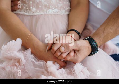 Ein zärtlicher Moment: Ineinander verflochtene Hände aus weichem rosa Stoff. Stockfoto