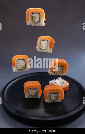 Schwimmende Lachsushi-Brötchen mit Frischkäse und Avocado in der Luft über dunklem Teller Stockfoto