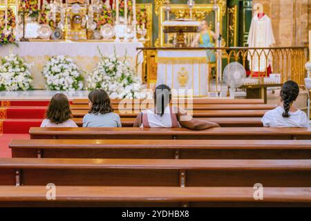 Touristen besuchen eine Messe in einer katholischen Kirche in Marbella, Spanien. Der Priester feiert die Messe vor dem Altar in MARBELLA, SPANIEN - 17. JULI 20 Stockfoto