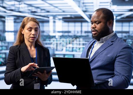 Team von Technikern im Serverraum, die einen Laptop verwenden, um Sicherheitsmaßnahmen zu implementieren und aufrechtzuerhalten und Systeme vor unbefugtem Zugriff zu schützen. IT-Spezialisten für Rechenzentren, die Hardware-Upgrades durchführen Stockfoto