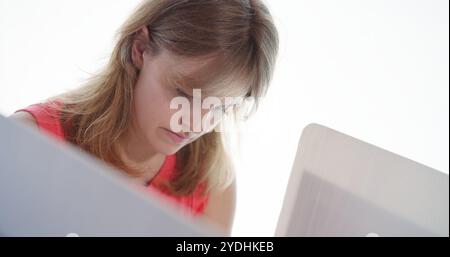Nahaufnahme einer jungen Frau, die nach unten blickt, während sie am Stand Stimmen abgibt und die Optionen überlegt. Abgewinkelter Blick von der Seite der Abstimmungskabine. Weißer Hintergrund b Stockfoto