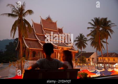 Luang Prabang; Laos - 8. April 2011: Silhouette zweier Kinder auf dem Hmong Nachtmarkt mit Haw Pha Bang Tempel im Hintergrund im Zentrum von Luang Stockfoto