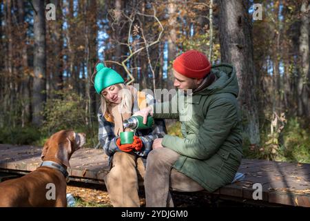 Ehepaar mittleren Alters mit Hund, der Tee trinkt, sitzt auf Ökotrop im Herbstpark Nordskandinavien. Stockfoto