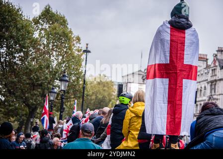 London, Großbritannien. Oktober 2024. Während der Demonstration wird ein Protestkörper mit dem Kreuz von England umhüllt. Tommy Robinson-Anhänger haben sich im Zentrum Londons zu einem Protest versammelt, den der politische Aktivist vermissen wird, nachdem er von der Polizei in Gewahrsam genommen wurde. Die Metropolitan Police hatte Robinson's Unite the Kingdom Kundgebung unter die Bedingung gestellt, dass sie ihre Prozession zum Parliament Square nicht vor 13:00 Uhr beginnen konnte. Credit: SOPA Images Limited/Alamy Live News Stockfoto