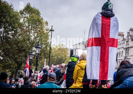 London, Großbritannien. Oktober 2024. Während der Demonstration wird ein Protestkörper mit dem Kreuz von England umhüllt. Tommy Robinson-Anhänger haben sich im Zentrum Londons zu einem Protest versammelt, den der politische Aktivist vermissen wird, nachdem er von der Polizei in Gewahrsam genommen wurde. Die Metropolitan Police hatte Robinsons Kundgebung Unite the Kingdom unter die Bedingung gestellt, dass sie ihre Prozession zum Parlamentsplatz nicht vor 13 Uhr beginnen konnte (Foto: Loredana Sangiuliano/SOPA Images/SIPA USA) Credit: SIPA USA/Alamy Live News Stockfoto