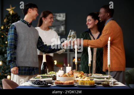 Verschiedene festliche Speisen auf dem Esstisch, dekoriert mit beleuchteten Kerzen, während die Leute Gläser anschlagen, Weihnachten im Hintergrund feiern, sich auf Geschirr konzentrieren, Kopierraum Stockfoto