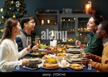 Seitenansicht einer Gruppe von Freunden mit Sektgläsern, die beim Plaudern zum Weihnachtsessen zu Hause anstoßen, Kopierraum Stockfoto