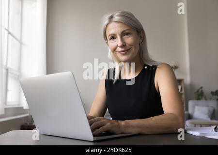 Porträt lächelnd selbstbewusste alte Dame sitzt am Schreibtisch am Laptop Stockfoto
