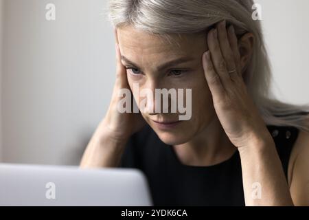 Älterer weiblicher Look auf dem Laptop-Bildschirm reiben die Schläfen in Chaos Stockfoto