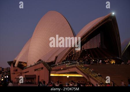Die hohen Segel der Konzerthalle des Sydney Opera House in der Abenddämmerung mit Menschen auf dem Geländer und monumentalen Stufen, die nach Osten in den Sonnenuntergang blicken Stockfoto