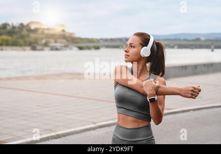 Athletische Kaukasierin in enger Sportswear und Kopfhörern, die vor einem Lauf in der Stadt Aufwärmübungen macht. Stockfoto