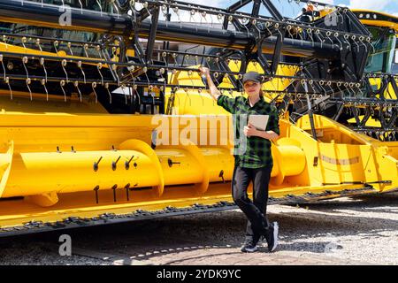 Eine Landwirtin oder Vertreterin des Landmaschinenhändlers steht neben dem neuen Mähdrescher mit einem digitalen Tablet in der Hand. Stockfoto