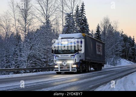 Der speziell angefertigte Scania Truck L Retva Oy zieht bei Dämmerung im Winter den Auflieger auf der Autobahn 52, während das helle Fernlicht kurz eingeschaltet ist. Salo, Finnland. Dezember 2021 Stockfoto