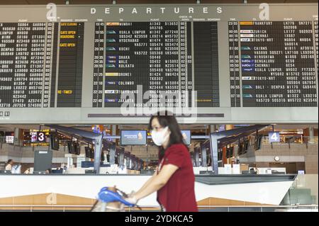 18.03.2020, Singapur, Republik Singapur, Asien, Eine Frau geht an einer Anzeigetafel mit Abfluginformationen in der Abflughalle von Terminal 2 vorbei Stockfoto