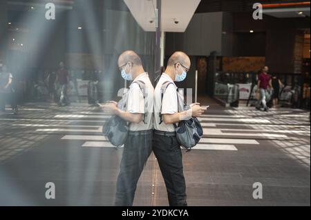 02.04.2020, Singapur, Republik Singapur, Asien, Ein Mann starrt sein Handy im Raffles City Einkaufszentrum an, während er eine Schutzmaske trägt Stockfoto